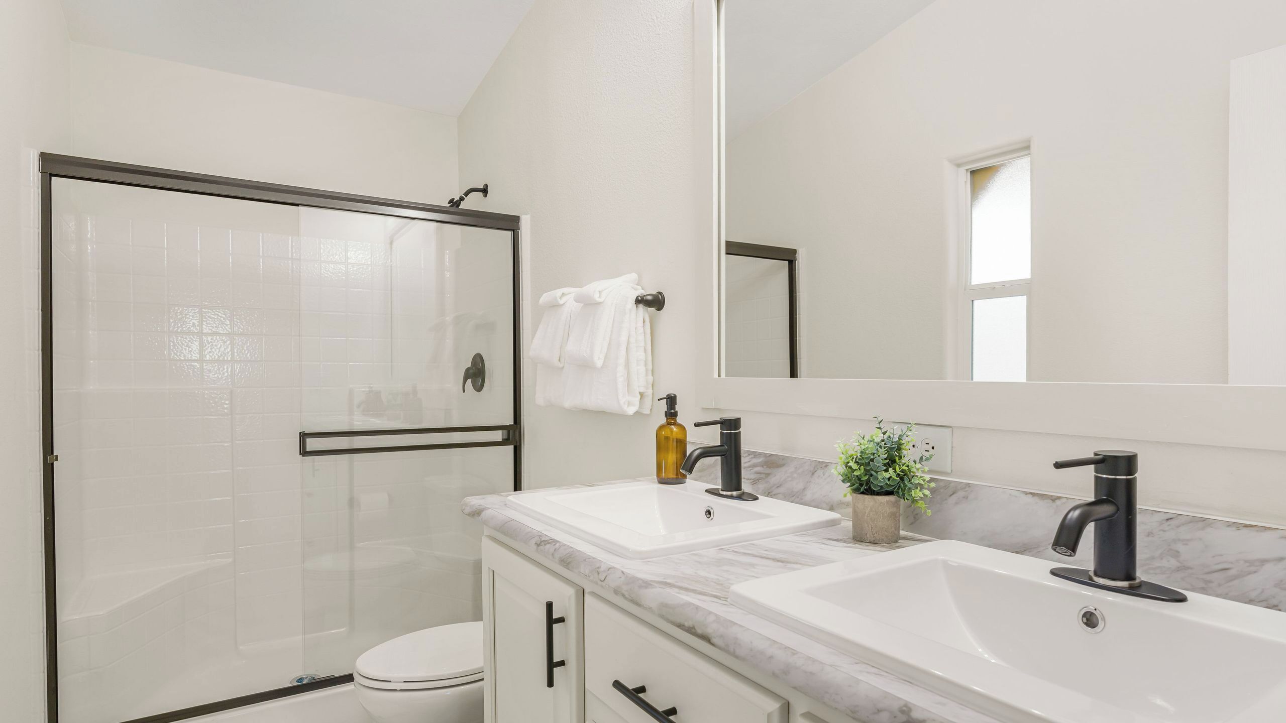 A modern bathroom with a glass shower enclosure, a toilet, a sink with a marble countertop, and a large mirror.