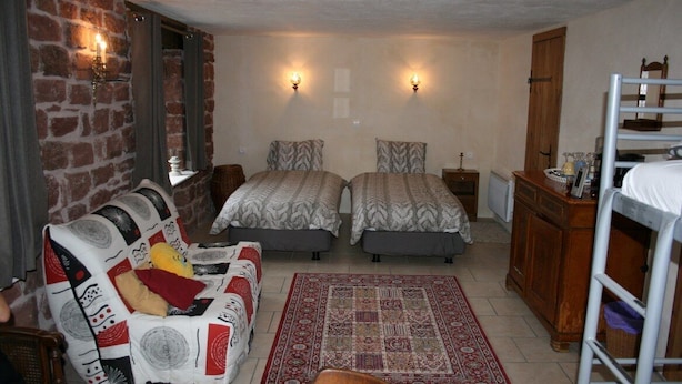 Une pièce avec deux lits, un canapé, une armoire en bois et un tapis rouge à motifs.