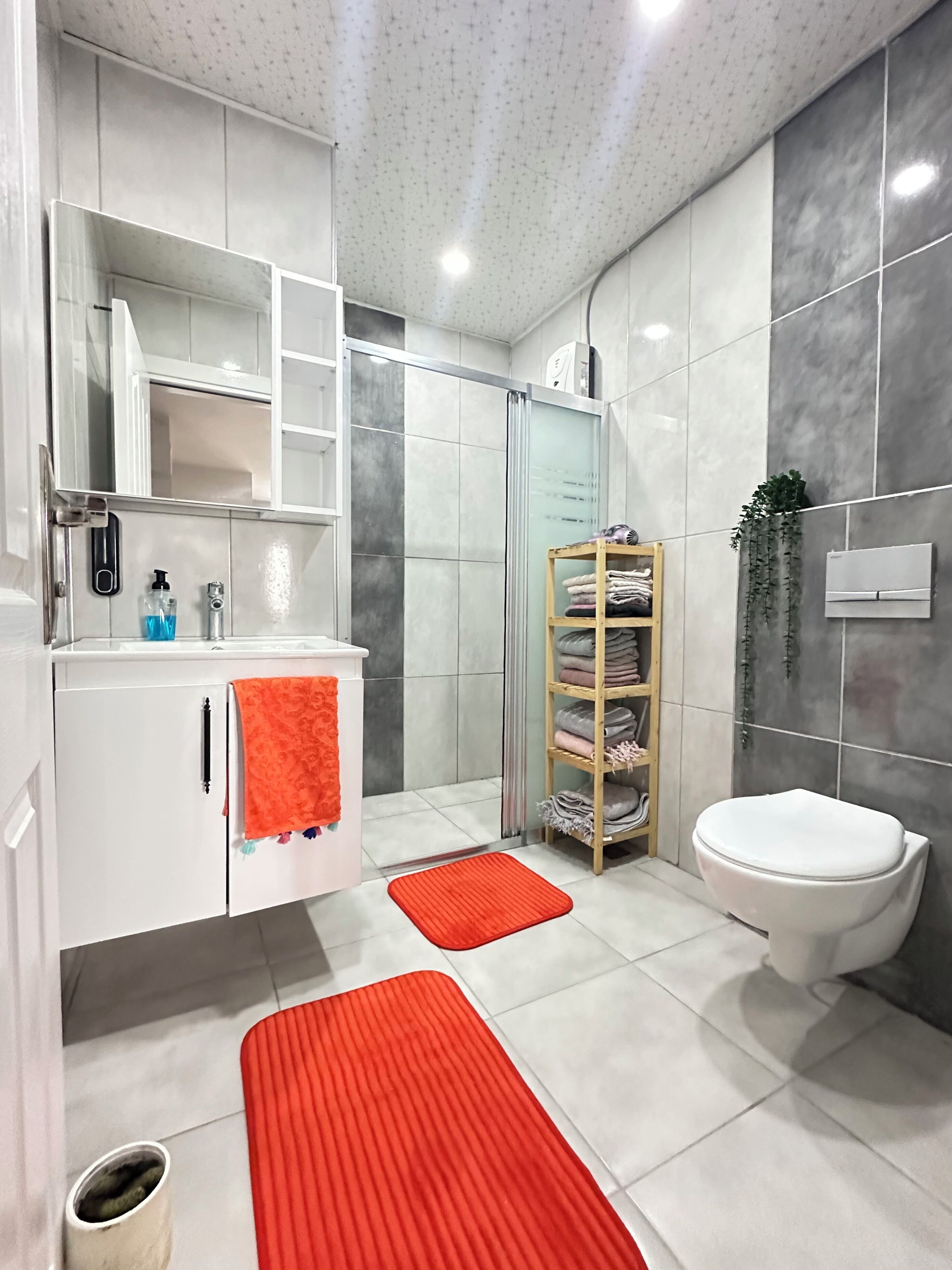A modern bathroom with a white vanity, a glass shower enclosure, a toilet, and a shelf with folded towels.