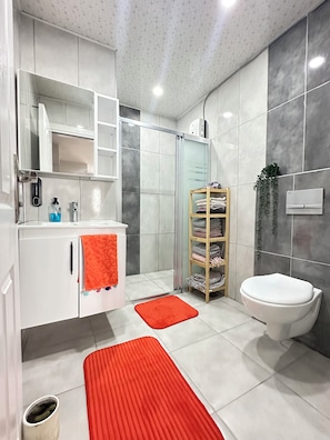 Une salle de bain moderne avec un meuble-lavabo blanc, une cabine de douche en verre, des toilettes et une étagère où sont pliées des serviettes.