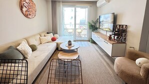En moderne stue med sofa, sofabord, fjernsyn og udsigt til en balkon.