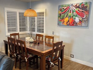 A dining area with a wooden table, chairs, a hanging light fixture, and a wall-mounted painting of spices. - Charming Valley Home, Close to Top LA Attractions; Lovely 3-bedroom house (Los Angeles)