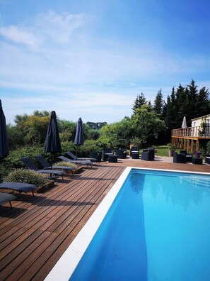 Una terraza de madera con piscina, sillas de descanso y sombrillas.