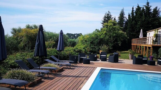 Um deck de madeira com piscina, cadeiras de descanso e guarda-sóis.