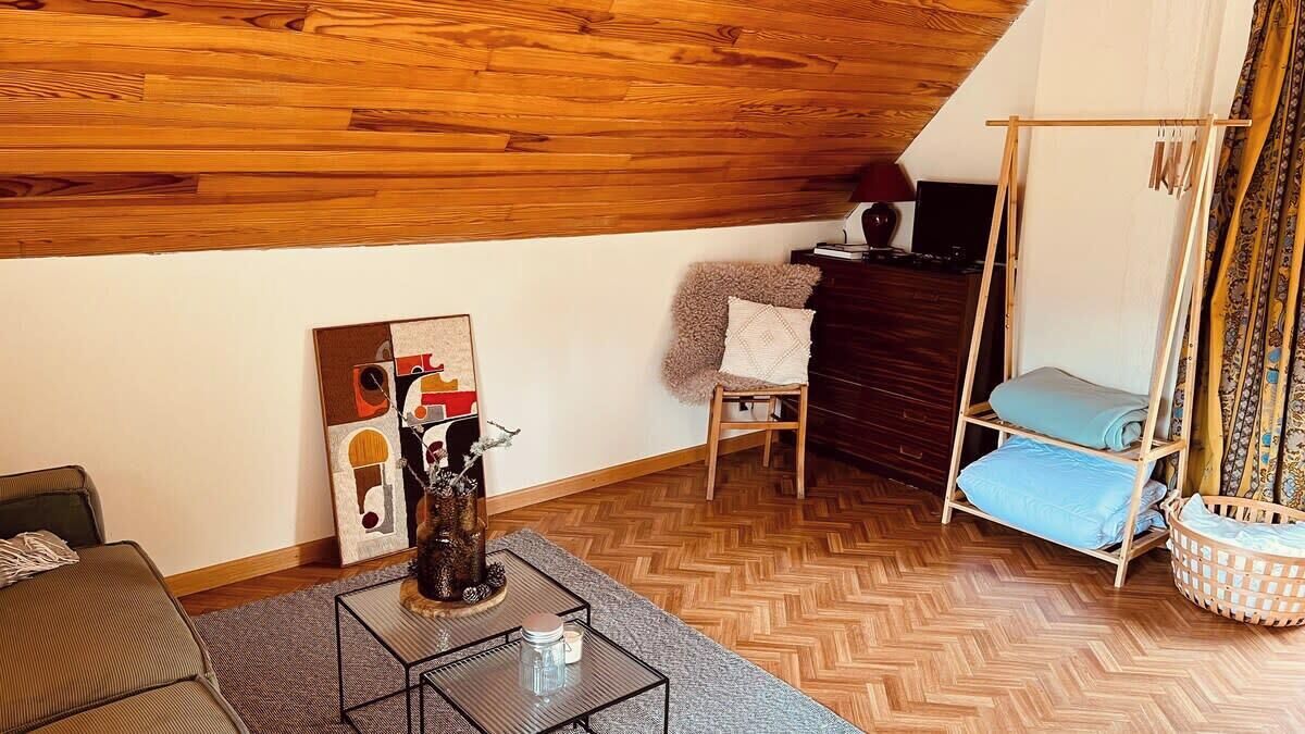 Une pièce chaleureuse avec un plafond en bois, un canapé, une table basse, un fauteuil, une petite table avec un vase et un fauteuil suspendu agrémenté de coussins.