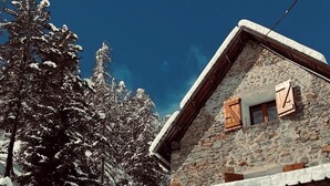 A snow-covered wooden cabin with a stone facade, a wooden balcony, and a clear blue sky. - Grange pour 6 personnes avec studio indépendant (Beuil)