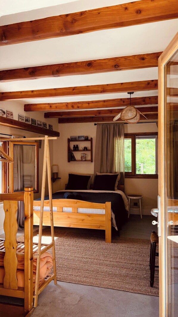 A bedroom with a wooden bed, a small table, a window with curtains, and a wooden ladder.