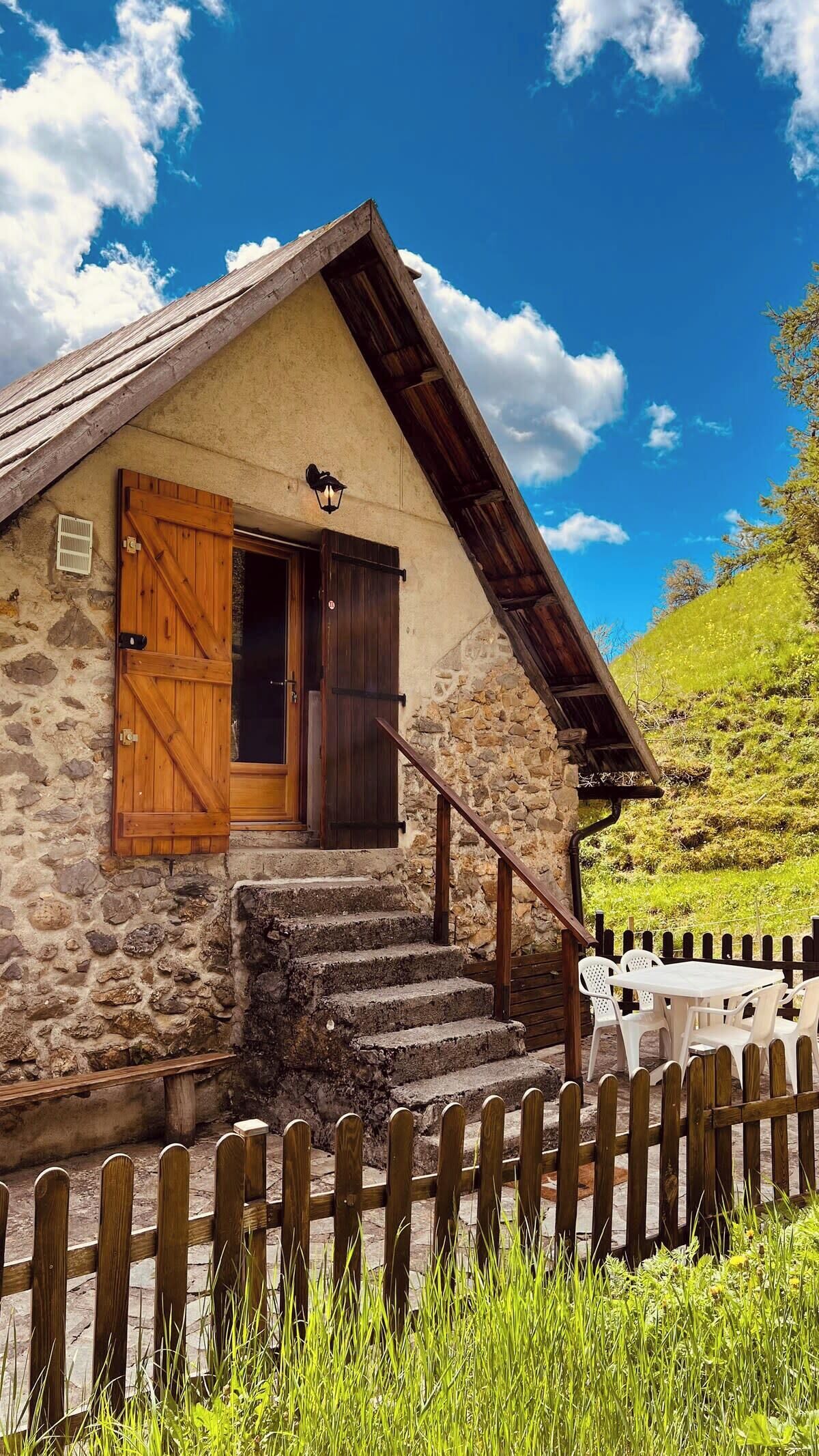 Une maison en pierre avec une porte en bois et des volets aux fenêtres, un escalier en pierre et une clôture en bois.