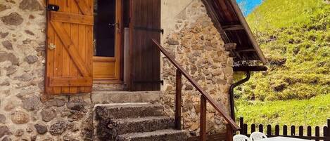 Une maison en pierre avec une porte en bois et des volets aux fenêtres, un escalier en pierre et une clôture en bois.