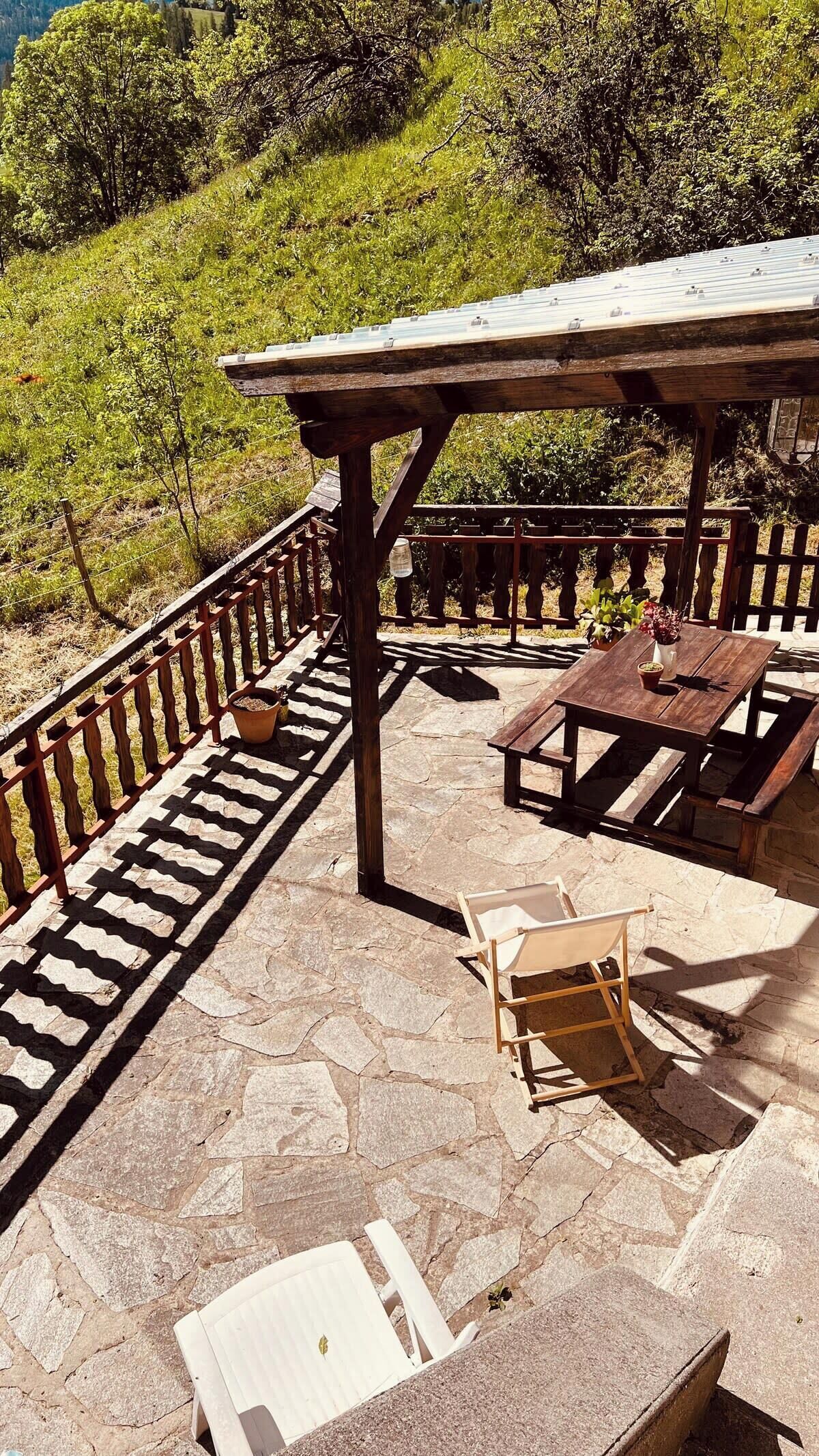 An outdoor patio with stone flooring, wooden furniture, and a pergola.