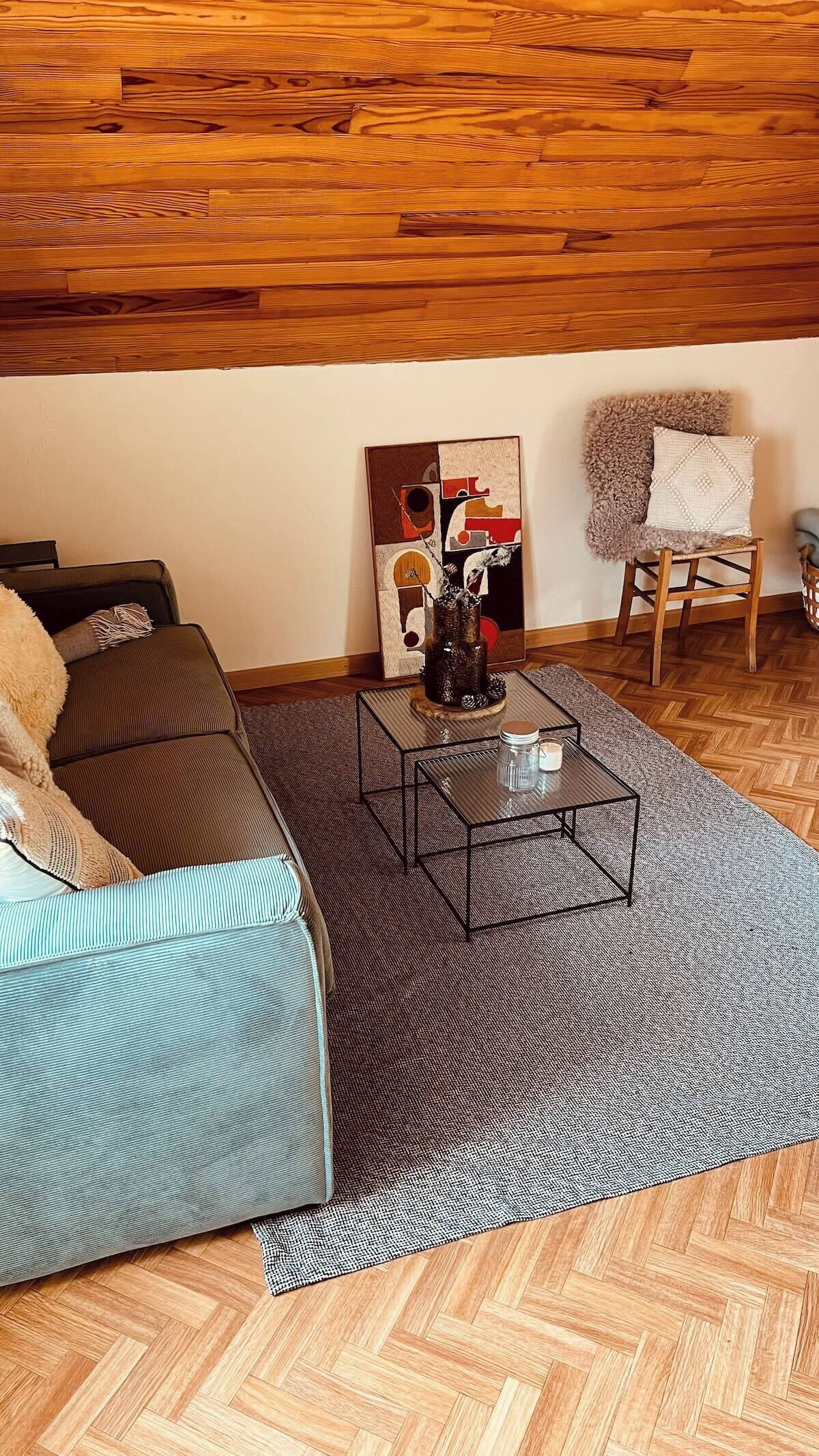 Una sala de estar con piso de madera en espiga, un sofá azul, una mesa de centro de vidrio y un cuadro en la pared.