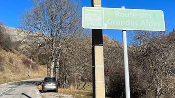 Segnaletica stradale per la Route des Grandes Alpes, con un cielo azzurro limpido e un'auto parcheggiata sul lato della strada.