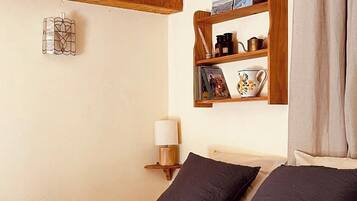 Une chambre à coucher avec un lit, des poutres en bois, une étagère avec des livres et des objets décoratifs, une lampe et une fenêtre avec des rideaux.