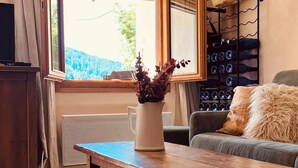 A cozy living room with a wooden table, a comfortable sofa, a small stool, and a window with curtains. - Belle grange éco responsable et cosy (Beuil)