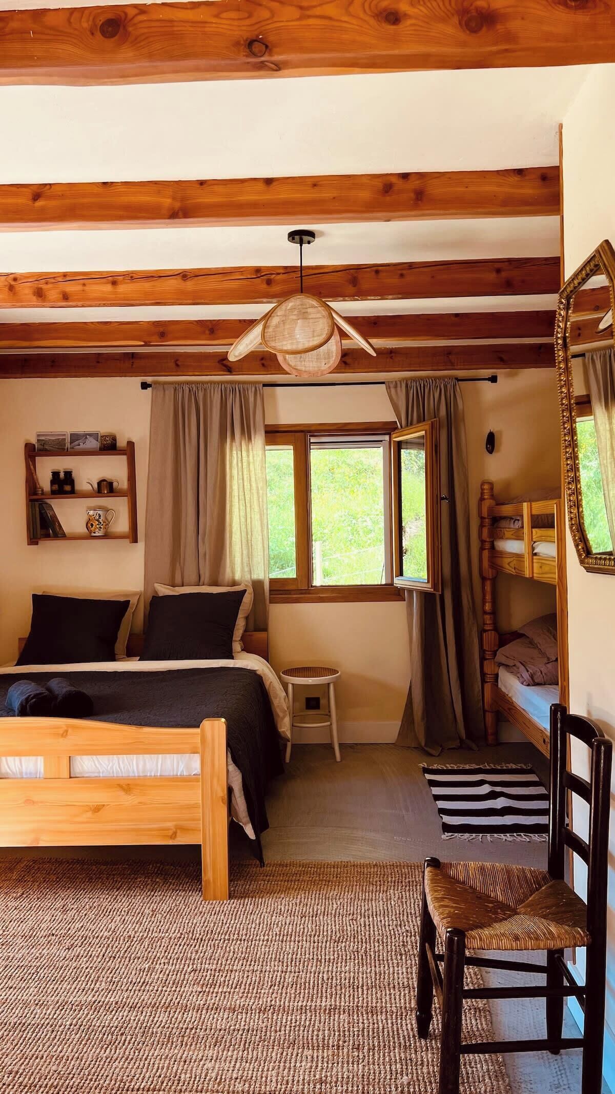 Une chambre confortable avec un lit en bois, un lit superposé, une petite table de chevet, une chaise et un miroir.