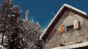 A stone cabin with a wooden balcony, surrounded by snow-covered trees and a snow-covered slope. - Belle grange éco responsable et cosy (Beuil)