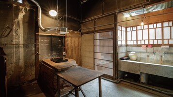 Una habitación rústica con una mesa de madera, una ventana con rejas y una lámpara.