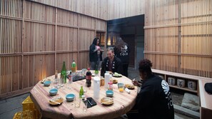 A round dining table with various dishes and drinks, surrounded by wooden walls with vertical slats. - Mitoyotsuru Toji by Toma Rutto (Mitoyo)