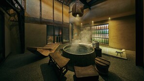 A traditional Japanese onsen with a wooden bench, a stone hot spring, and a shelf of green bottles. - Mitoyotsuru Toji by Toma Rutto (Mitoyo)