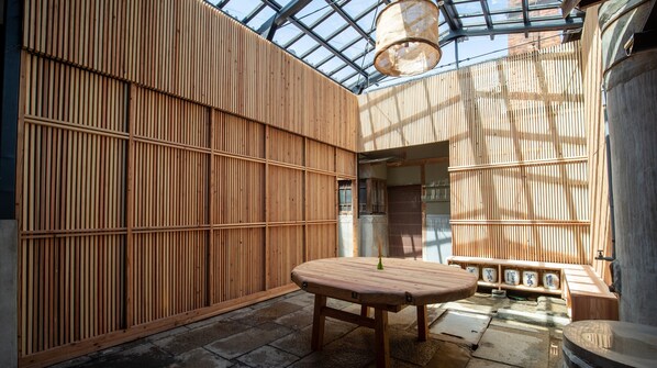 A room with a wooden slatted wall, a table, and a hanging light fixture. - Mitoyotsuru Toji by Toma Rutto (Mitoyo)