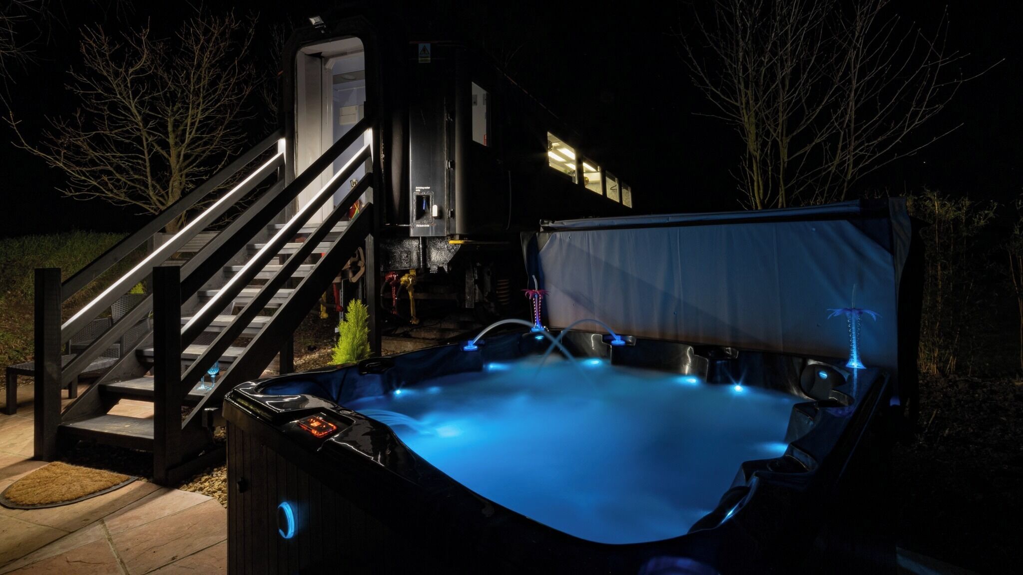 A hot tub with a blue light, a staircase, and a covered area.