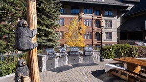 Une terrasse extérieure agrémentée d’une sculpture d’ours en bois, d’un barbecue en pierre et d’une table en bois.