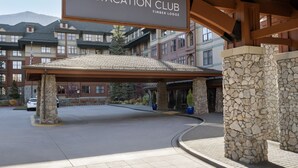 L’entrée d’un hôtel, dotée d’un espace abrité, de piliers en pierre et d’une enseigne indiquant « Vacation Club Timber Lodge ».