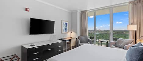 A hotel room with a large bed, a desk, a chair, a TV, and a view of the city.