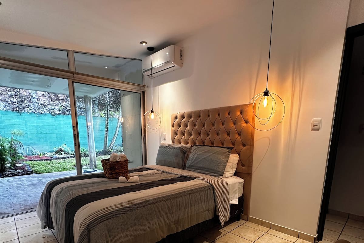 A bedroom with a large bed, a view of the outdoors, and a modern design.