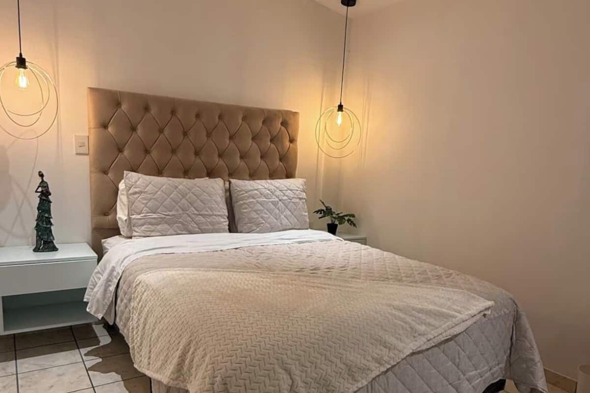 A bedroom with a tufted headboard, a large bed with a quilted bedspread, two bedside tables, and a nightstand with a small plant.
