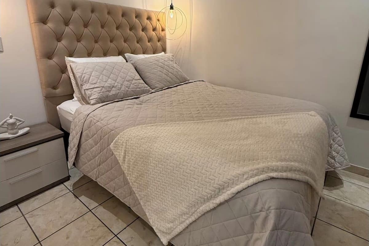 A bedroom with a tufted headboard, a quilted bedspread, and a bedside table with a lamp.