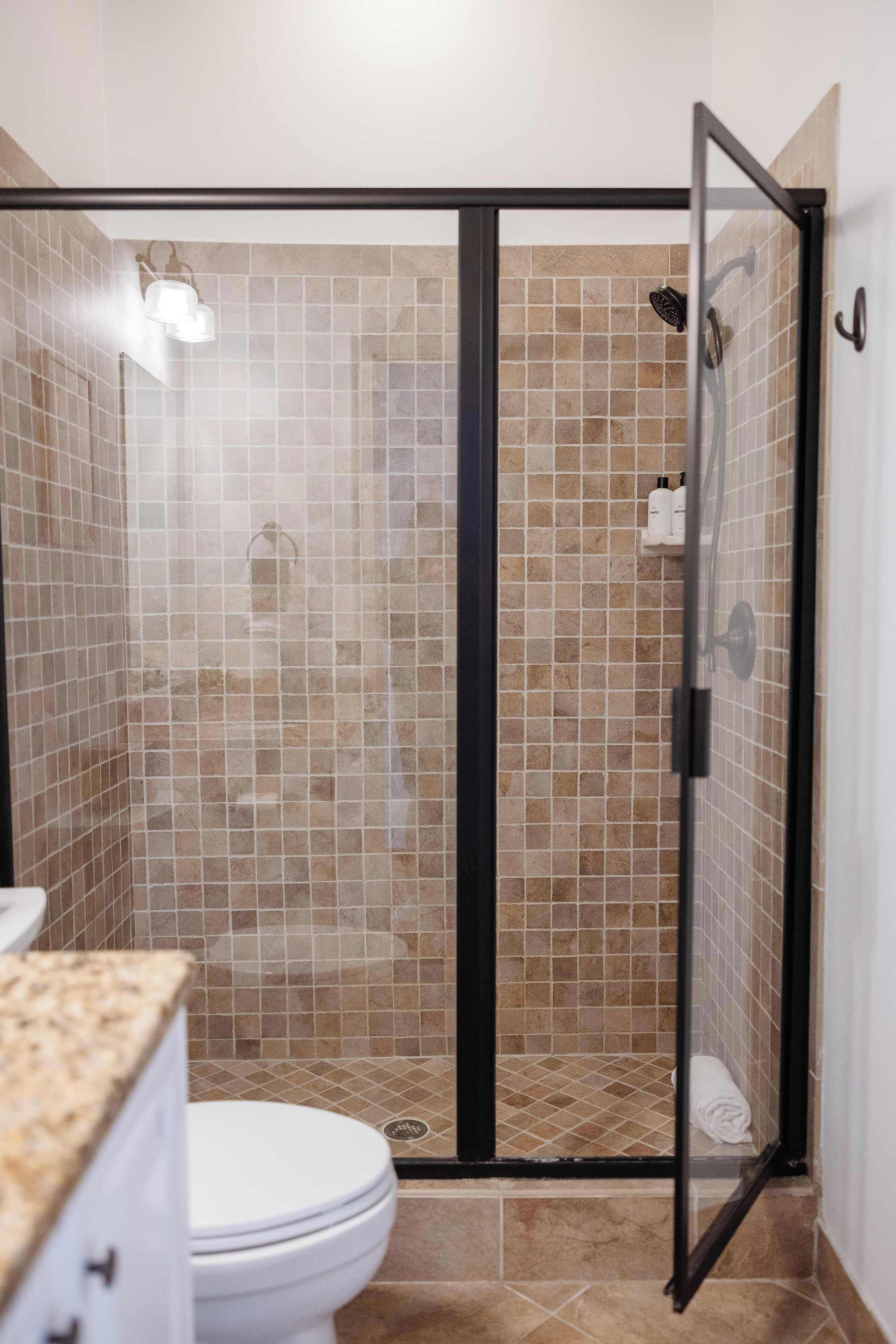 Una ducha a nivel con puerta de vidrio, paredes de azulejos color beige y un inodoro blanco en primer plano.
