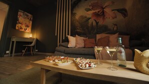 A cozy living room with a sofa, a dining table with snacks and drinks, and a painting on the wall.