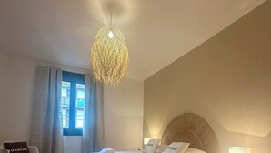 Une chambre d’hôtel avec un grand lit, une table de chevet avec une lampe, une chaise avec un coussin et une fenêtre avec des rideaux.