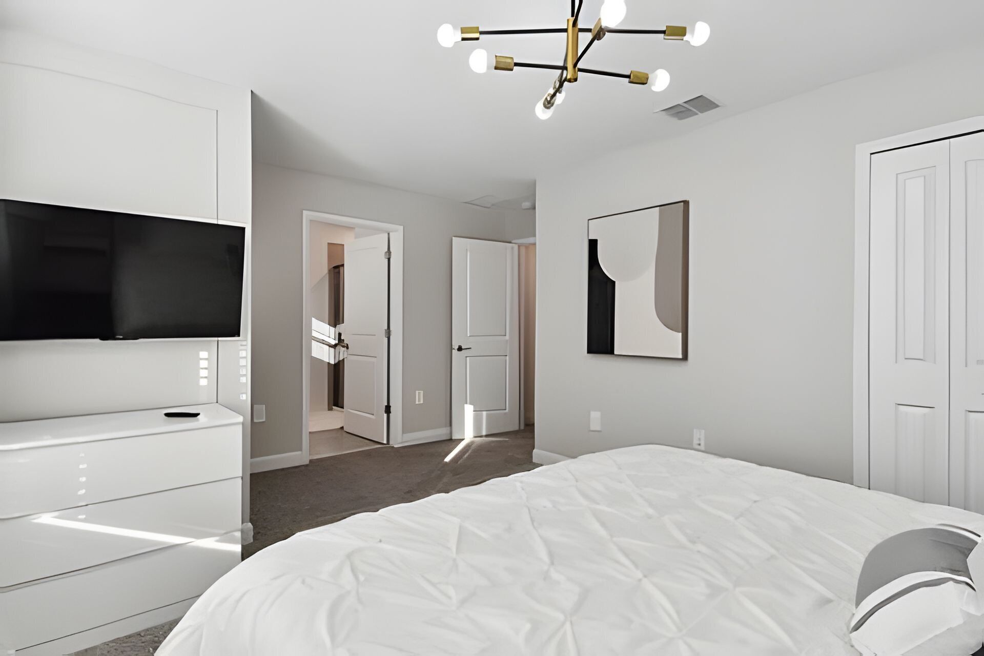 Un dormitorio moderno con una cama grande, un televisor montado en una cómoda y una lámpara de techo.