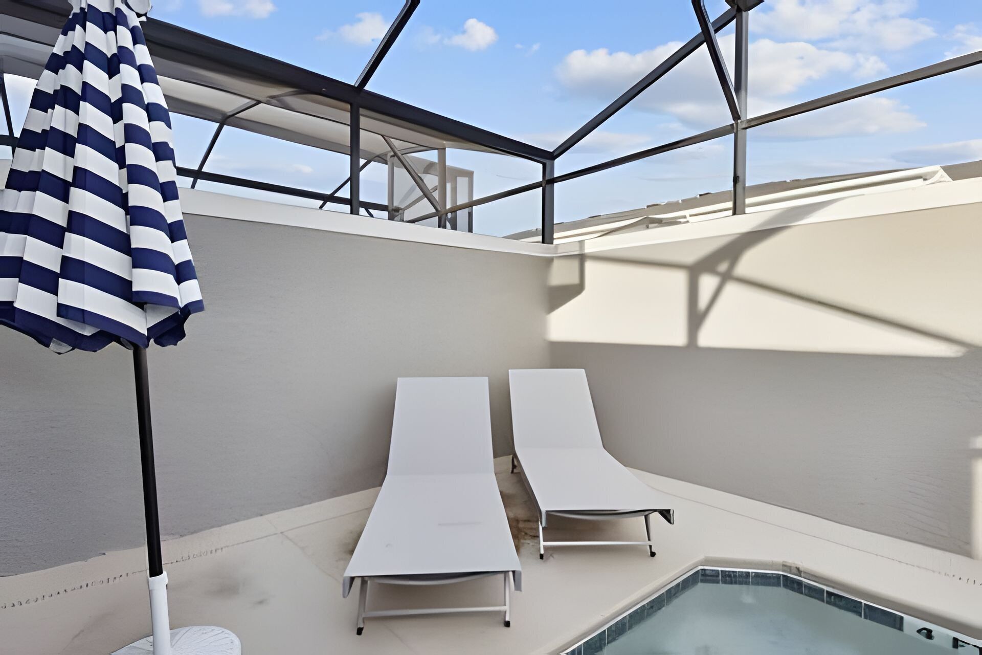 A poolside area with two lounge chairs and a striped umbrella.