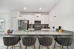 A modern kitchen with white cabinets, stainless steel appliances, and a central island with bar stools. - Storey Lake 5bd/4ba Private Pool Near Disney (Kissimmee)