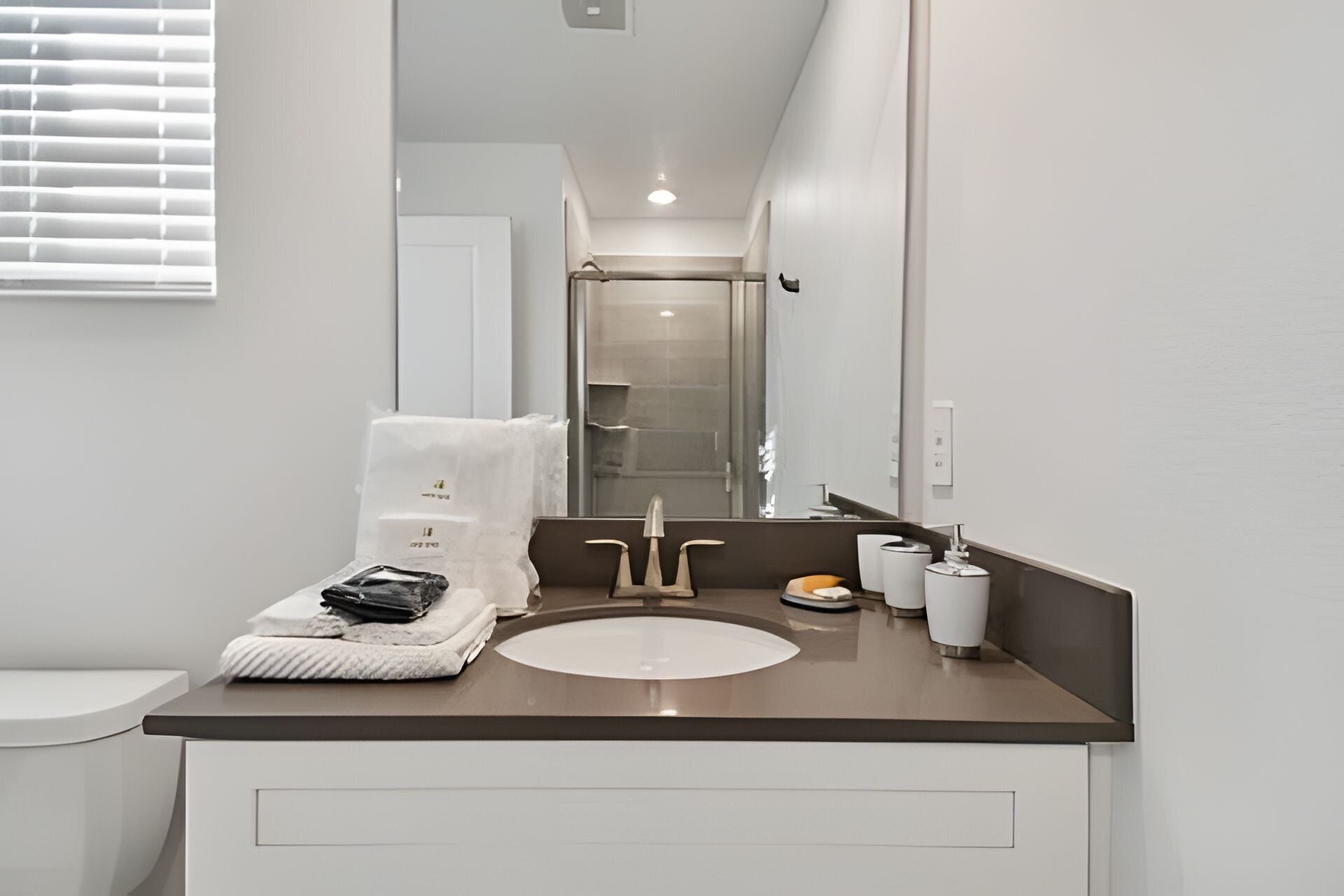 A modern bathroom with a white sink, two faucets, a mirror, and a towel rack.