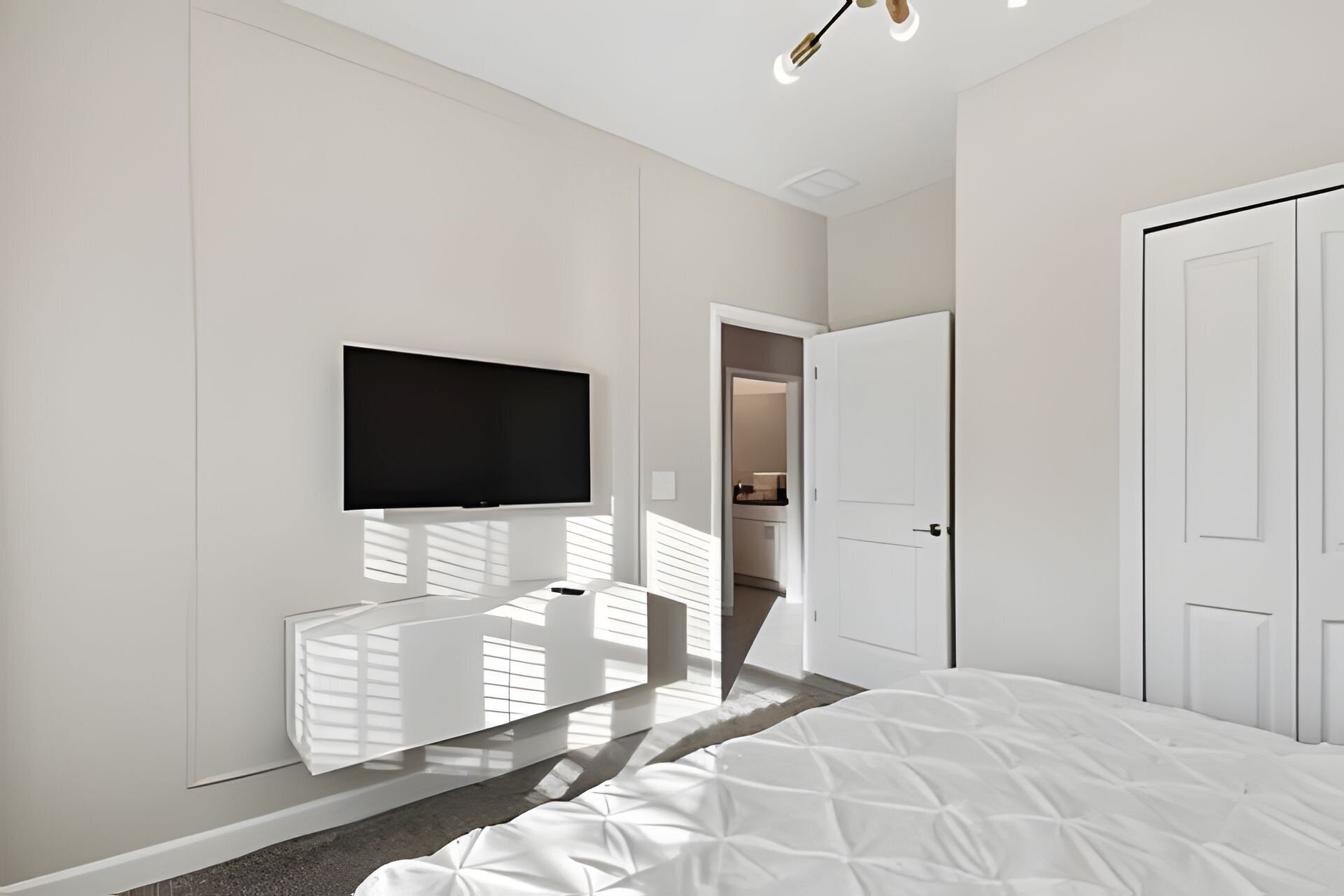 A modern bedroom with a large bed, a mounted TV, and a wardrobe.