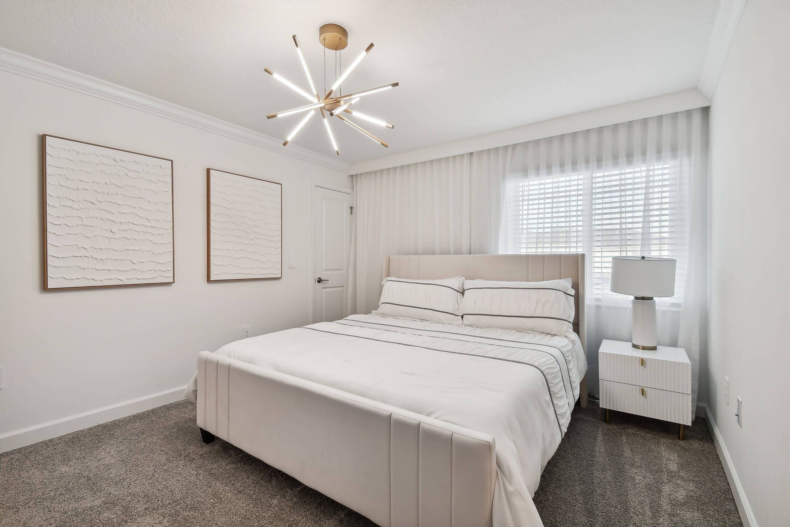 A modern bedroom with a large bed, a bedside table with a lamp, and two framed artworks on the wall.