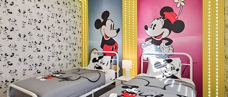 Une chambre d’enfant avec deux lits, chacun décoré avec des motifs de Mickey Mouse. La chambre est dotée d’un papier peint à motifs et d’un mur d’accent d’un rose vif.