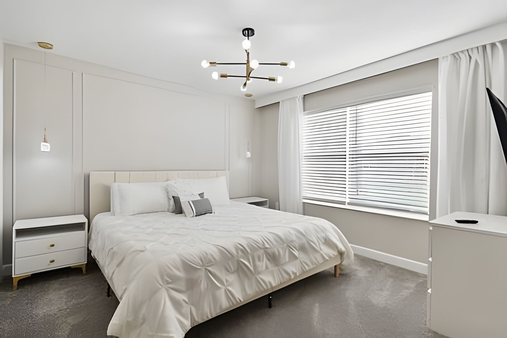 Een moderne slaapkamer met een groot bed, nachtkastjes, een bureau en een raam met zonwering.