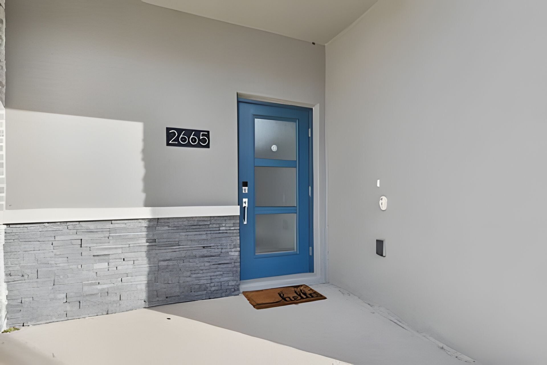 A building entrance with a blue door, a stone wall, and a number sign.