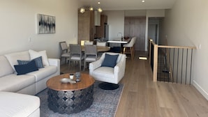 Un salon moderne avec un canapé, des fauteuils, une table basse et un coin repas comprenant des chaises, avec une cuisine en arrière-plan.