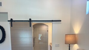 Une chambre à coucher comprenant un lit, une table de chevet avec une lampe, une porte coulissante donnant accès à une salle de bain et un élément de décoration circulaire fixé au mur.