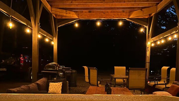 Een zone met een jacuzzi, houten balken, lichtjes en buitenmeubilair.
