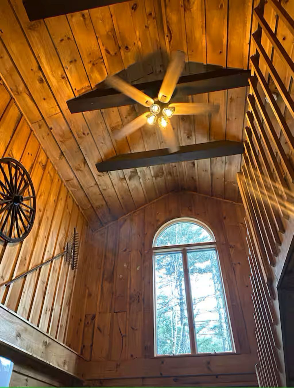 L’intérieur d’une cabane avec des murs en bois, un plafond en pente, un ventilateur de plafond, une fenêtre donnant sur la forêt et une porte en bois rustique.