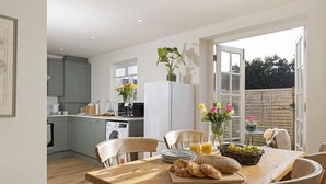 Eine moderne Küche mit grauen Schränken, einer Waschmaschine und einer Essecke mit einem Holztisch, gedeckt für das Frühstück.
