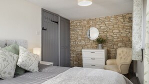 Ein Schlafzimmer mit Stehwänden, einem Bett mit Blumenbettwäsche, einem Sessel, einem Schminktisch und einem Spiegel.