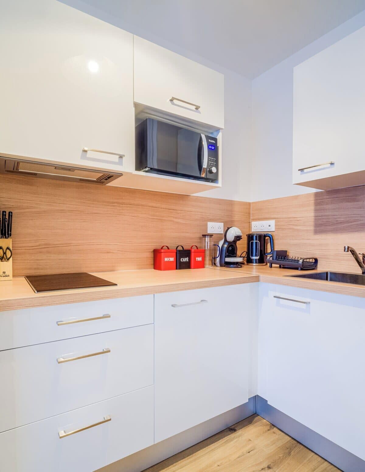 A modern kitchen with white cabinets, a microwave, a coffee maker, and a toaster.